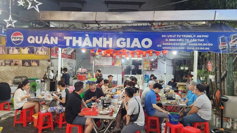 Khu ăn ngoài trời đông khách dưới bảng hiệu xanh